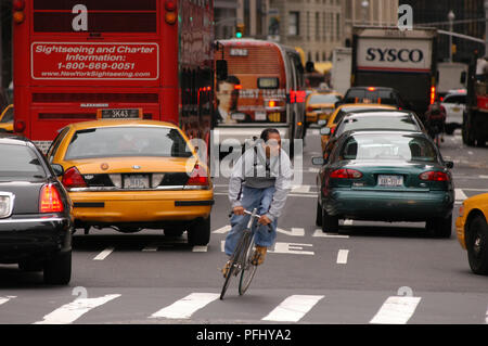 Nord America, USA, New York City, 59th Street Broadway, uomo su una bicicletta tra il traffico Foto Stock