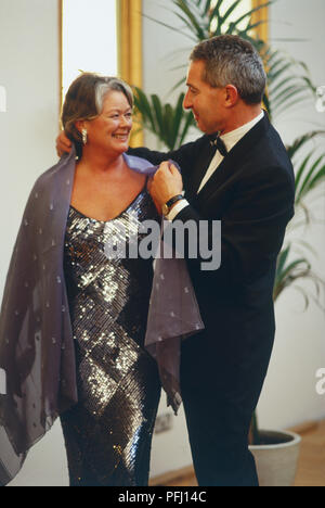 Uomo maturo ad aiutare la donna con il suo scialle Foto Stock