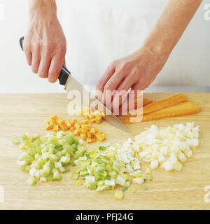 Cipolla, porro, il sedano e le carote tagliate a dadini essendo sul tagliere di legno, vista frontale Foto Stock