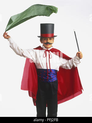 Ragazzo che indossa un mantello rosso, baffi e un top hat, tenendo un bastone in una mano e oscillazione un pezzo di velo verde sopra la testa con l'altra mano Foto Stock