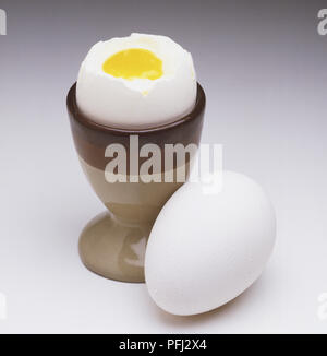 Un uovo sodo, con la sua parte superiore rimosso in un uovo e una tazza e un uovo intero accanto ad esso Foto Stock