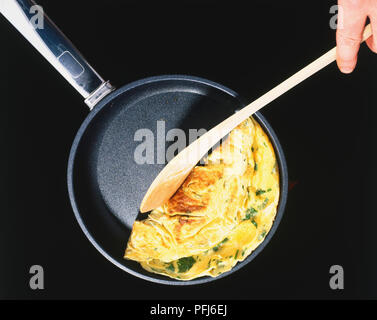 La frittata in una padella antiaderente essendo piegato a metà con un cucchiaio di legno, vista da sopra. Foto Stock
