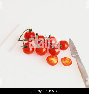 Vite stagionati pomodori ciliegia e il coltello sul tagliere, uno di loro tagliato a metà. Foto Stock