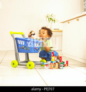 Ragazzo giocando con il giocattolo carrello per supermercati, tenendo su vaso piccolo. Foto Stock