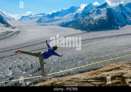 Giovane donna è in equilibrio su slackline presso il Rifugio Konkordia sopra il ghiacciaio ghiaccio a Konkordiaplatz, Alpi Bernesi, Vallese, Svizzera Foto Stock