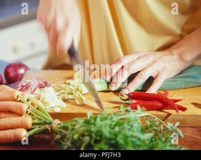 Essendo il porro tagliato a fettine su tagliere di legno, accanto a fette di cipolle rosse, tutto il peperoncino rosso e il mazzetto di carote. Foto Stock