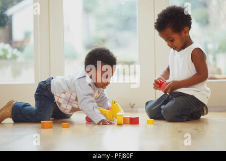 Due bambini seduti sul pavimento in legno nella parte anteriore della porta di patio giocando con il giocattolo morbido e cubi Foto Stock