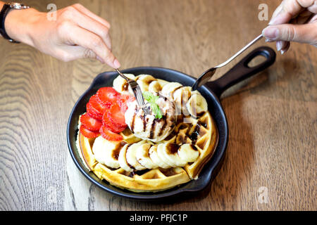 Mano che tiene la forcella mangiare chiacchiere con gelato alla vaniglia e frutta fresca in un ristorante di tabella Foto Stock