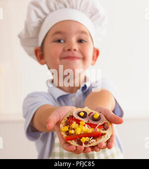 Ragazzo in chef hat mostra crudo pizza pitta, close-up Foto Stock
