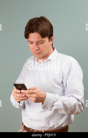 Digitare il messaggio. Bel giovane con capelli afro in camicia di contenimento del telefono mobile Foto Stock