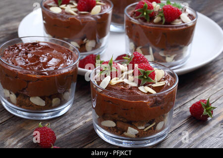 Deliziosa mousse al cioccolato in bicchieri di vetro con biscotti al cioccolato e decorate con foglie di menta, lamponi e scaglie di mandorle sul piatto bianco sul vecchio dar Foto Stock