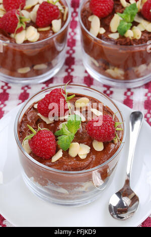 Deliziosa mousse al cioccolato in bicchieri di vetro e rabboccato con foglie di menta fresca, lamponi e scaglie di mandorle sulla piastra bianca con cucchiaio su carta asciugatutto, clo Foto Stock
