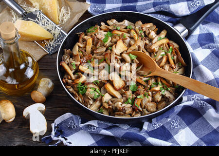 Funghi trifolati o porcini fritti cosparsa di prezzemolo in padella con asciugamano da cucina in legno scuro tavolo. fresco intero ceps, parmigiano e Foto Stock