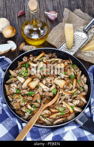 Funghi trifolati o porcini fritti cosparsa di prezzemolo in padella con asciugamano da cucina in legno scuro tavolo. fresco intero ceps, parmigiano e Foto Stock