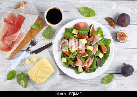 Fresh baby spinaci, fichi, tagliate a fette sottili di prosciutto italiano e gara mozzarella insalata di formaggio sulla piastra bianca di legno sul piano di lavoro della cucina con ingredienti su ba Foto Stock