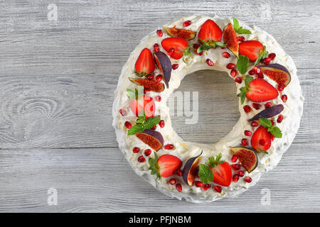 Deliziosa torta pavlova corona francese di meringa e panna montata, decorato con Fragola, fichi, i semi di melograno e menta su vecchie tavole di legno, Foto Stock