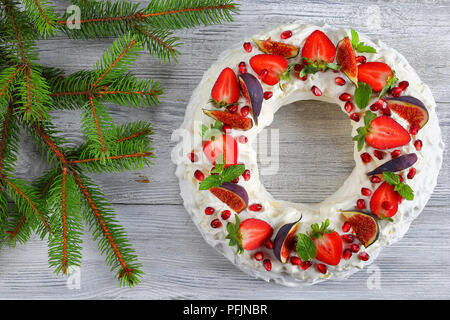 Deliziosa torta pavlova corona francese di meringa e panna montata, decorato con Fragola, fichi, melograni e menta sulla vecchia tabella con natale Foto Stock