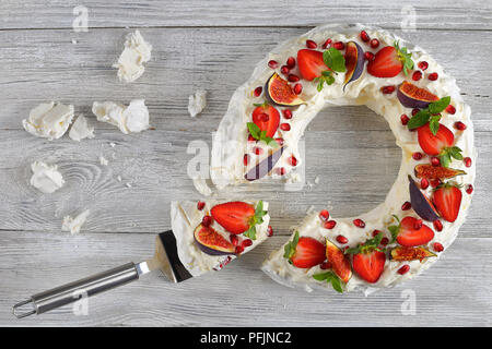 Pavlova cake corona francese di meringa e panna montata, decorato con Fragola, fichi, i semi di melograno e menta tagliata a fettine e un pezzo su c Foto Stock