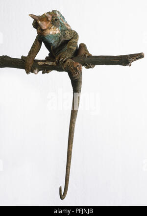 Jackson (Camaleonte Chamaeleo jacksonii) appollaiato sul ramo di albero con la sua lunga coda penzolante verso il basso in vista frontale Foto Stock