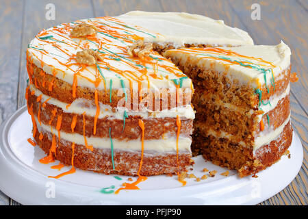 Classico deliziosa torta di carote con glassa di formaggio cremoso decorate con noci e spruzzata con glassa colorata con fetta tagliata sul piatto sul wo Foto Stock