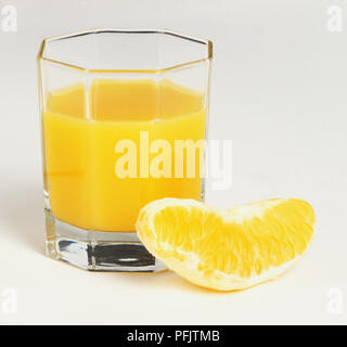 Vetro contenente succo di arancia, fetta d'arancia accanto al vetro Foto Stock