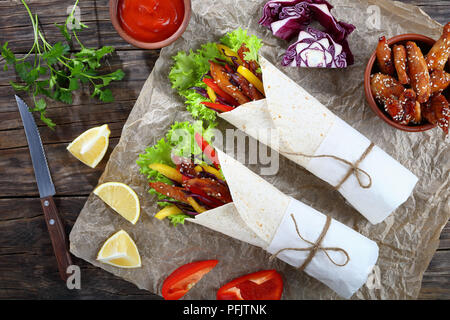 Appena fatti avvolgimenti a sandwich con frisee lattuga, peperoni, coleslaw e fritto glassato al miele bastoncini di pollo su carta. ingredienti a sfondo, vi Foto Stock