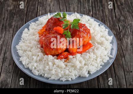 Close-up di gustosi piatti caldi con le polpette di pollo brasato in salsa di pomodoro con carote, cipolle, pastinaca e spezie, servito con riso a grani lunghi su una lastra grigia su Foto Stock