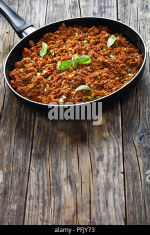 Hot succosa carne ragù alla bolognese con salsa di pomodoro, il basilico tritato finemente le verdure e il sedano in padella sul vecchio tavolo in legno, ricetta classica, vertica Foto Stock