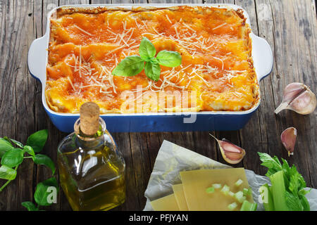 Le lasagne italiane conditi con formaggio fuso e di foglie di basilico fresco e cosparsi di parmigiano grattugiato in una teglia. autentica ricetta, close-up Foto Stock