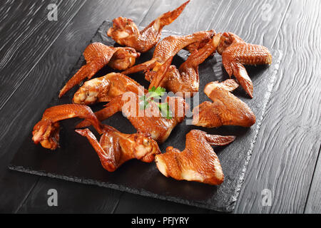 Deliziosi affumicato croccanti ali di pollo su una pietra nera della piastra sulla tavola di legno, vista da sopra Foto Stock