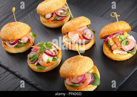 Delizioso piccolo hamburger segnato con gli spiedini di bambù o pinchos con gamberi, calamari, cozze, rosso anelli di cipolla e tritate finemente il cetriolo su ardesia tr Foto Stock