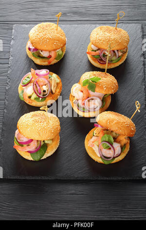 Deliziosi hamburger segnato con gli spiedini di bambù o pinchos con gamberi, calamari, cozze, rosso anelli di cipolla e tritate finemente il cetriolo sul nero ardesia tr Foto Stock