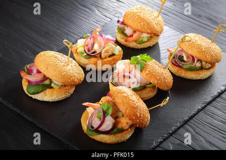 Deliziosi hamburger grigliati segnato con gli spiedini di bambù o pinchos con frutti di mare, cipolla rossa e verde su nero ardesia vassoio sul tavolo di legno, Spagna cucina, Foto Stock