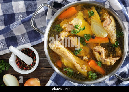 Cancellare il brodo di pollo con pezzi di intervallo libero Biologico di fattoria gallo sulla carne di osso in una casseruola di metallo con carta asciugatutto e ingredienti su legno tabl Foto Stock