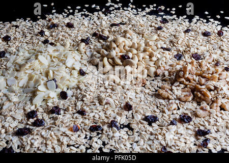 Granola INGREDIENTI Farina di avena fiocchi di mandorle sgusciate Noci e anacardi su sfondo nero dal lato Foto Stock