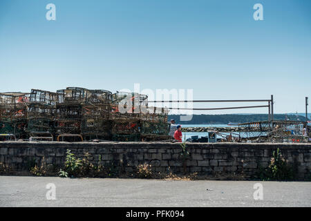 Granchi e aragoste bicchieri impilati sul quay accanto a Poole Harbour, con un uomo e ragazzo in background, Poole, Dorset, Regno Unito Foto Stock