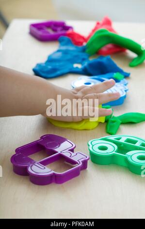 Bambino la mano sul pezzo di argilla giocare, stampi di plastica nelle vicinanze, close-up Foto Stock