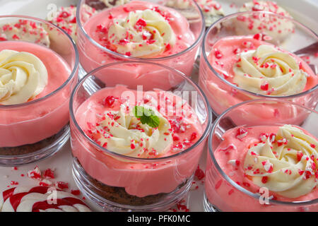 Close-up di Natale non cuocere Strawberry Cheesecake Mousse conditi con panna montata e cosparsi di schiacciate candy canes in bicchieri di vetro Foto Stock