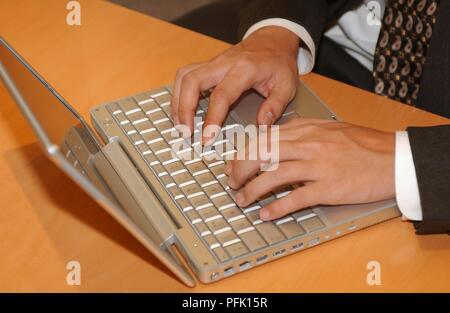 Imprenditore seduto alla scrivania e digitando su un piccolo portatile Foto Stock