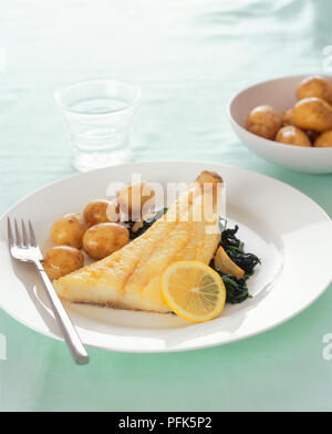 Eglefino con saltata di spinaci e patate bollite, su un piatto e una ciotola di patate bollite e un bicchiere di acqua Foto Stock