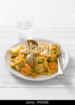 Fideua, spagnolo un piatto di pasta di spaghetti, Misto mare e piselli, servito con un bicchiere di acqua, close-up Foto Stock