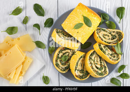 Deliziosi involtini di uova con un morbido ripieno di mix di spinaci, formaggio feta e carote tagliate a fettine su lastra grigia su un tavolo di legno con ingredienti a backgrou Foto Stock