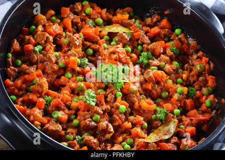 Close-up di deliziosi piatti classici con ragù di carne macinata, verdure, i piselli e i pomodori in padella - ingrediente principale per la pasta bolognese o pastore o Foto Stock