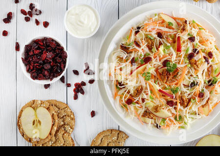 Close-up di Apple di mirtillo palustre e noci insalata Coleslaw su una piastra bianca sul tavolo di legno con mela rossa, fette biscottate multigrain, salsa di yogurt e Foto Stock