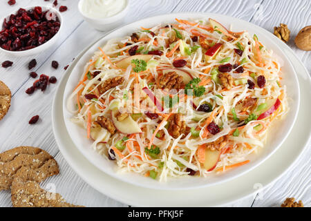 Apple mirtillo palustre e noci insalata Coleslaw su una piastra bianca sul tavolo di legno con ingredienti, multigrain pani croccanti e salsa di yogurt a sfondo, vista Foto Stock