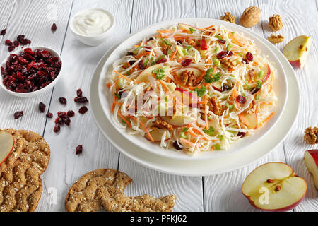 Apple mirtillo palustre e noci insalata Coleslaw su una piastra bianca sul tavolo di legno con mela rossa, fette biscottate multigrain, salsa di yogurt e i dadi a bac Foto Stock