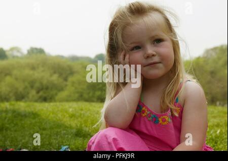 Ragazza in abito rosa seduta sul prato con la sua testa con le mani, close-up Foto Stock