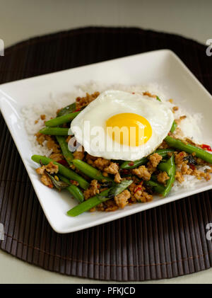 Pad kaprao gai, stir-fritto di pollo piccante con fagiolini, basilico tailandese e guarnita con uovo fritto Foto Stock