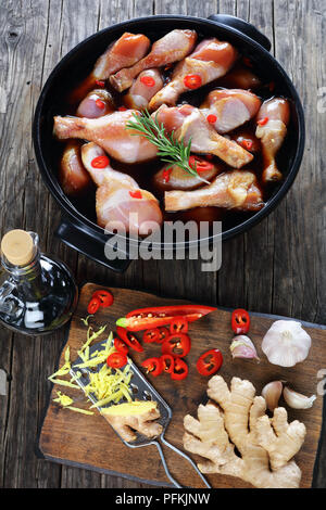 Il pollo crudo marinato bacchette con fatti in casa piccante salsa teriyaki in nero piatto. ingredienti sul tagliere di legno sul tavolo di legno, vista verticale Foto Stock