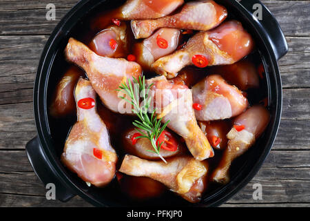 Il pollo crudo marinato bacchette con fatti in casa piccante salsa teriyaki in pot nero., vista da sopra, close-up Foto Stock